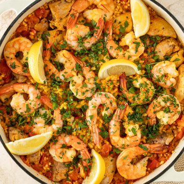 Paella mit Hähnchen und Garnelen, garniert mit frischer Petersilie und Zitronenspalten, in einer großen Pfanne.