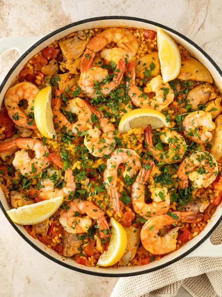 Paella mit H&auml;hnchen und Garnelen, garniert mit frischer Petersilie und Zitronenspalten, in einer gro&szlig;en Pfanne.