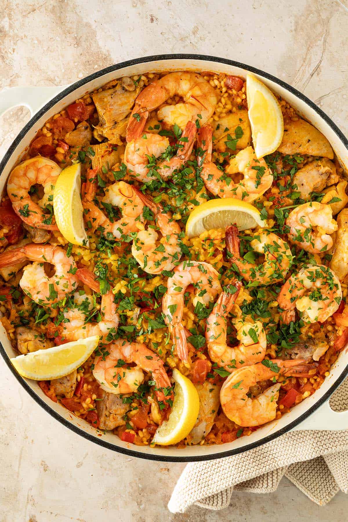 Paella mit Hähnchen und Garnelen, garniert mit frischer Petersilie und Zitronenspalten, in einer großen Pfanne.