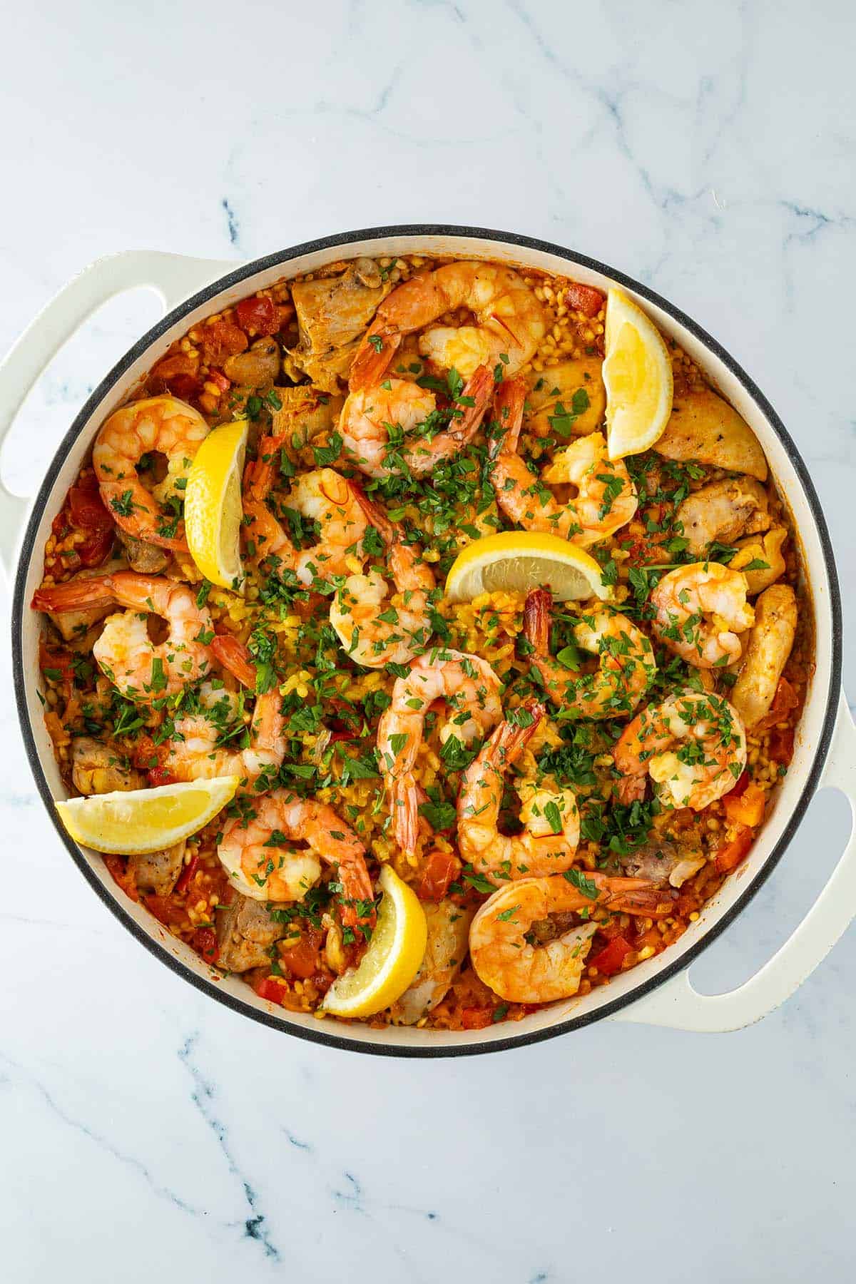Fertige Paella mit Hähnchen, Garnelen, Paprika und Safranreis, mit Petersilie und Zitronenspalten garniert.