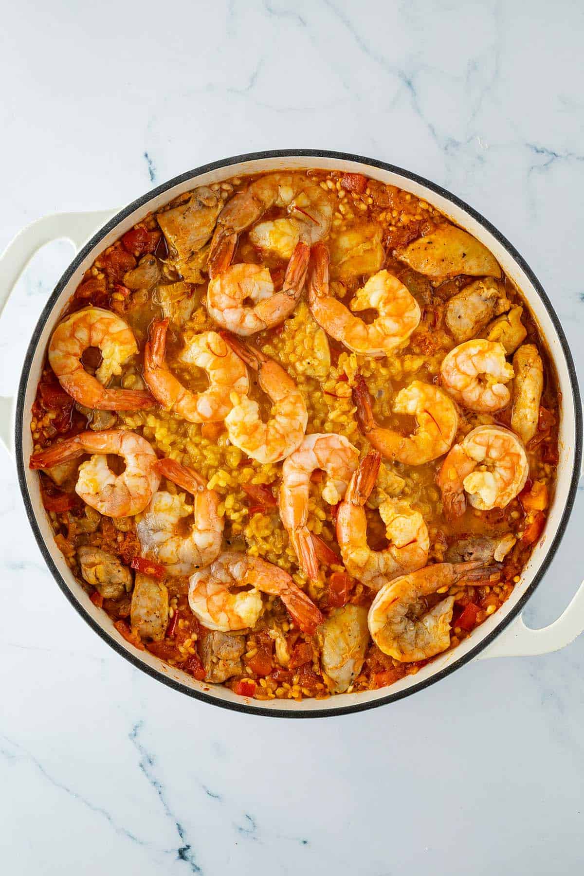 Paella mit Safranreis, Hähnchen und Garnelen auf der Oberfläche während des Garens in einer großen Pfanne.