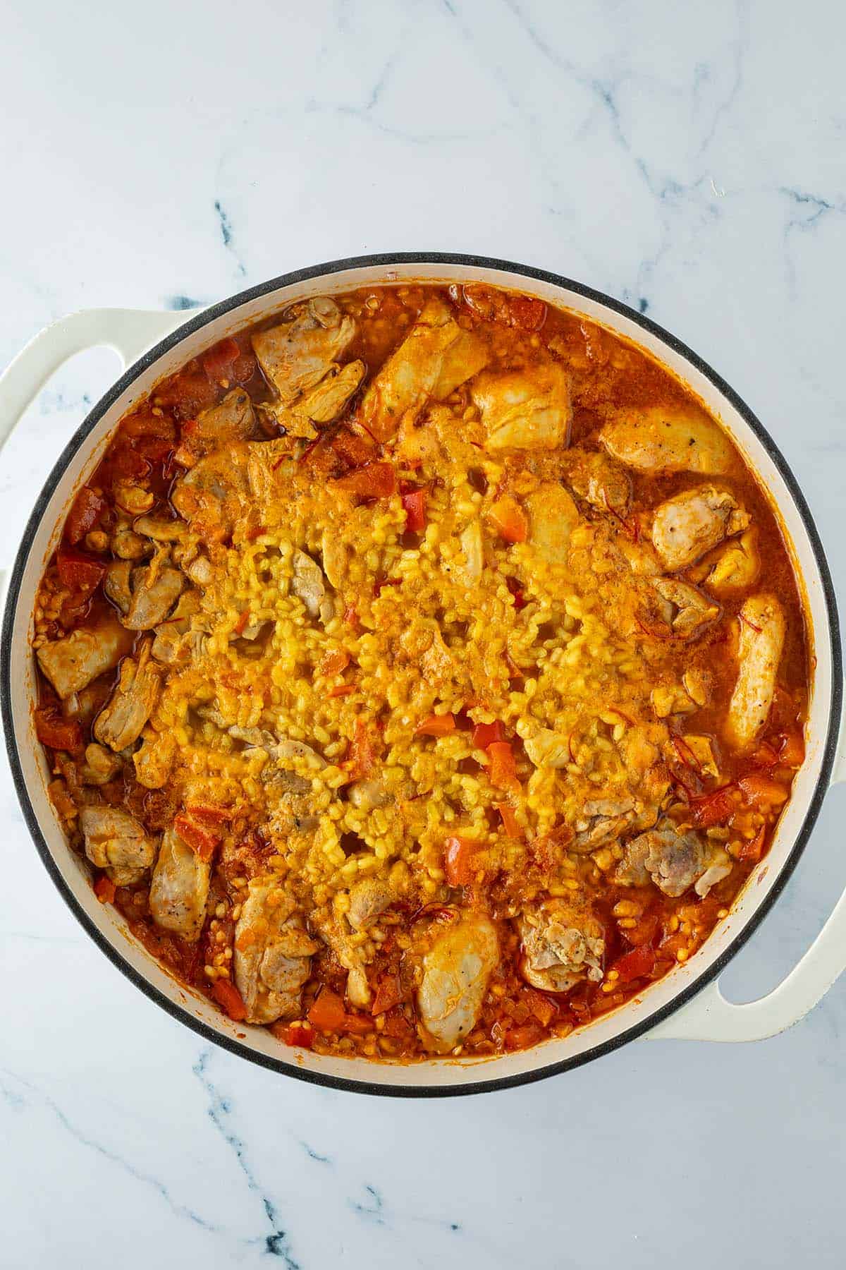 Paella mit Hähnchen und Safranreis während des Garens, bevor die Garnelen hinzugefügt werden.