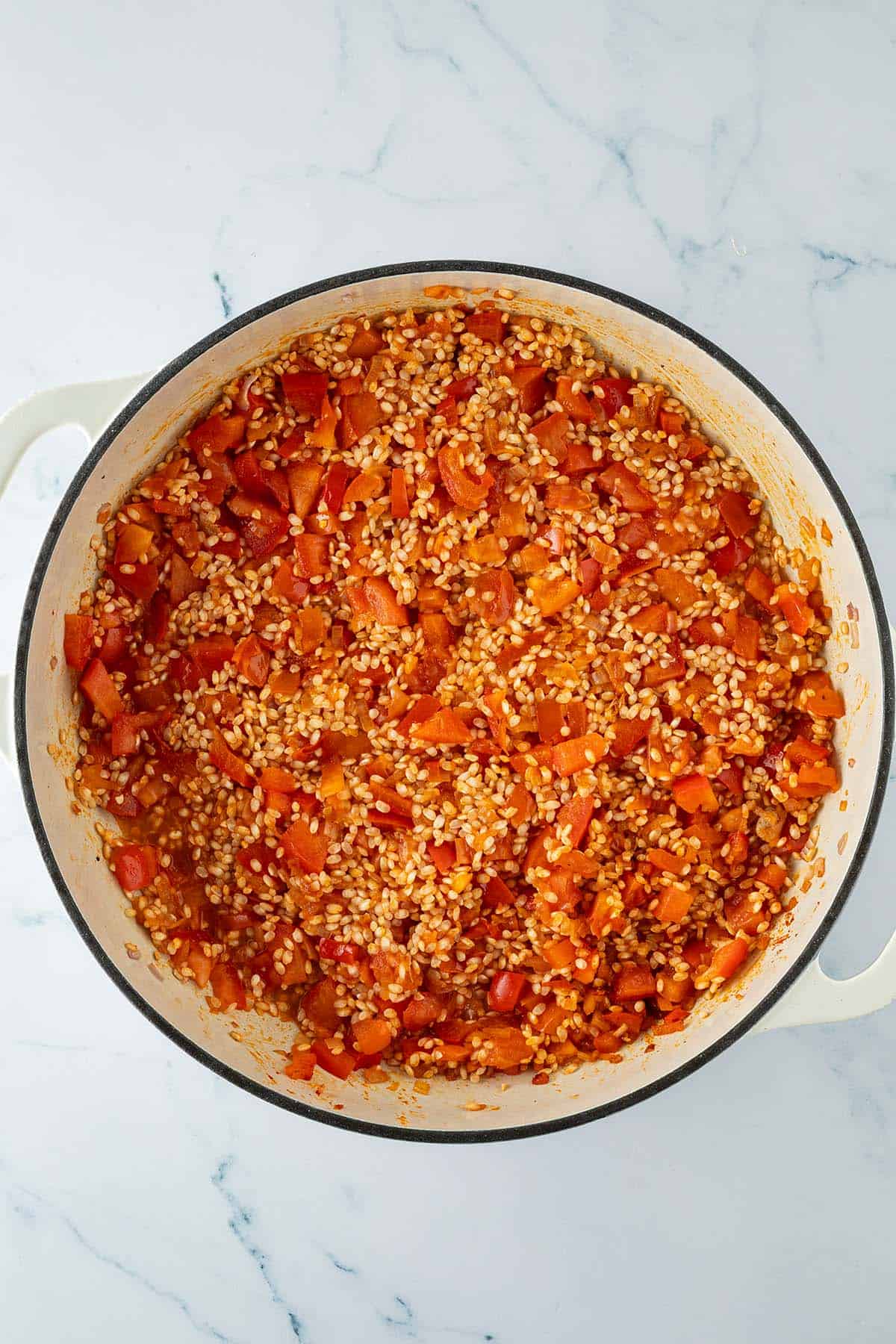 Paella-Reis mit gewürfelter Paprika und Tomaten in einer großen Pfanne nach dem Ablöschen mit Wein.