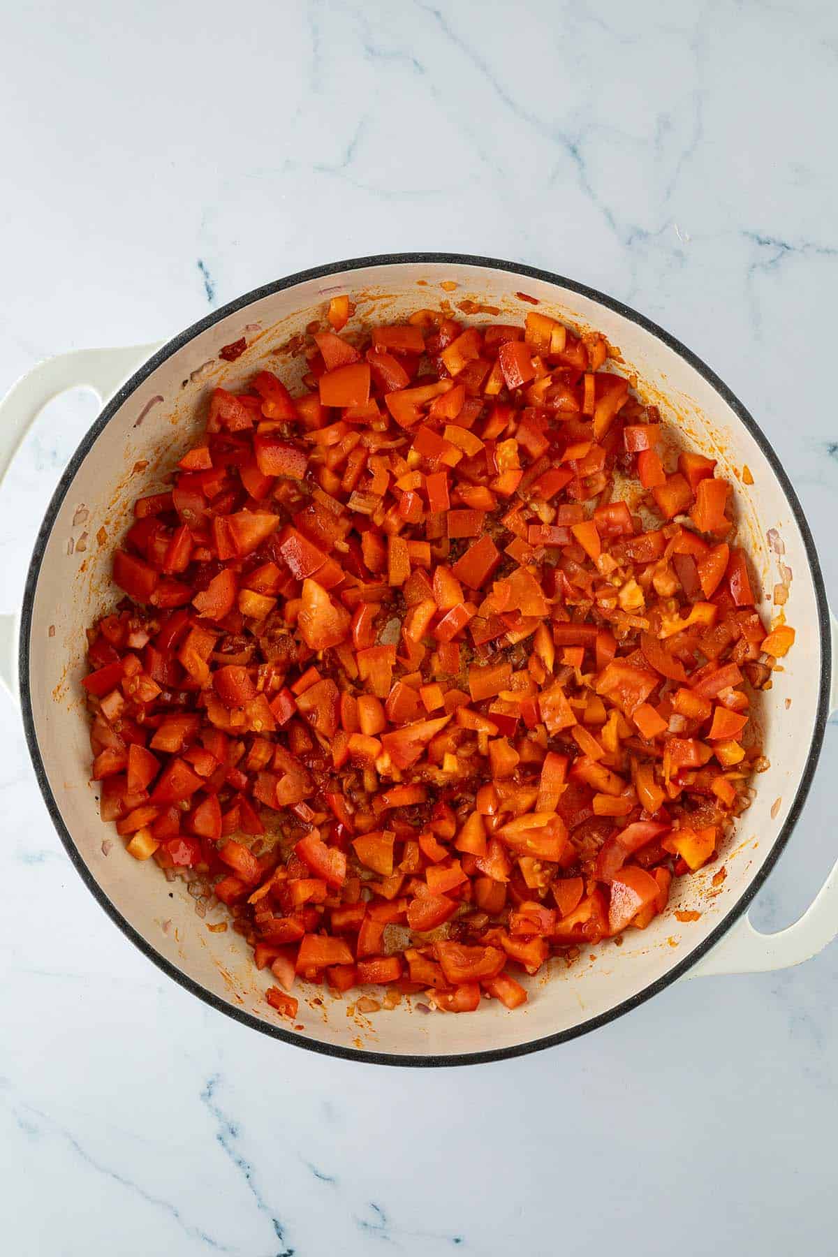 Angebratene Paprika, Tomaten und Zwiebeln als Gemüsegrundlage für Paella in einer großen Pfanne.
