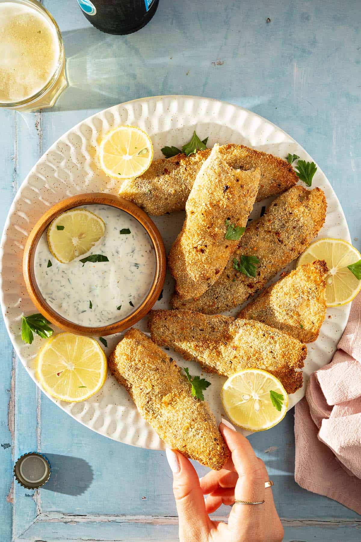 Teller mit mehreren panierten Fischfilets aus dem Airfryer, Zitronenscheiben und Kräuter-Dip, von oben fotografiert.