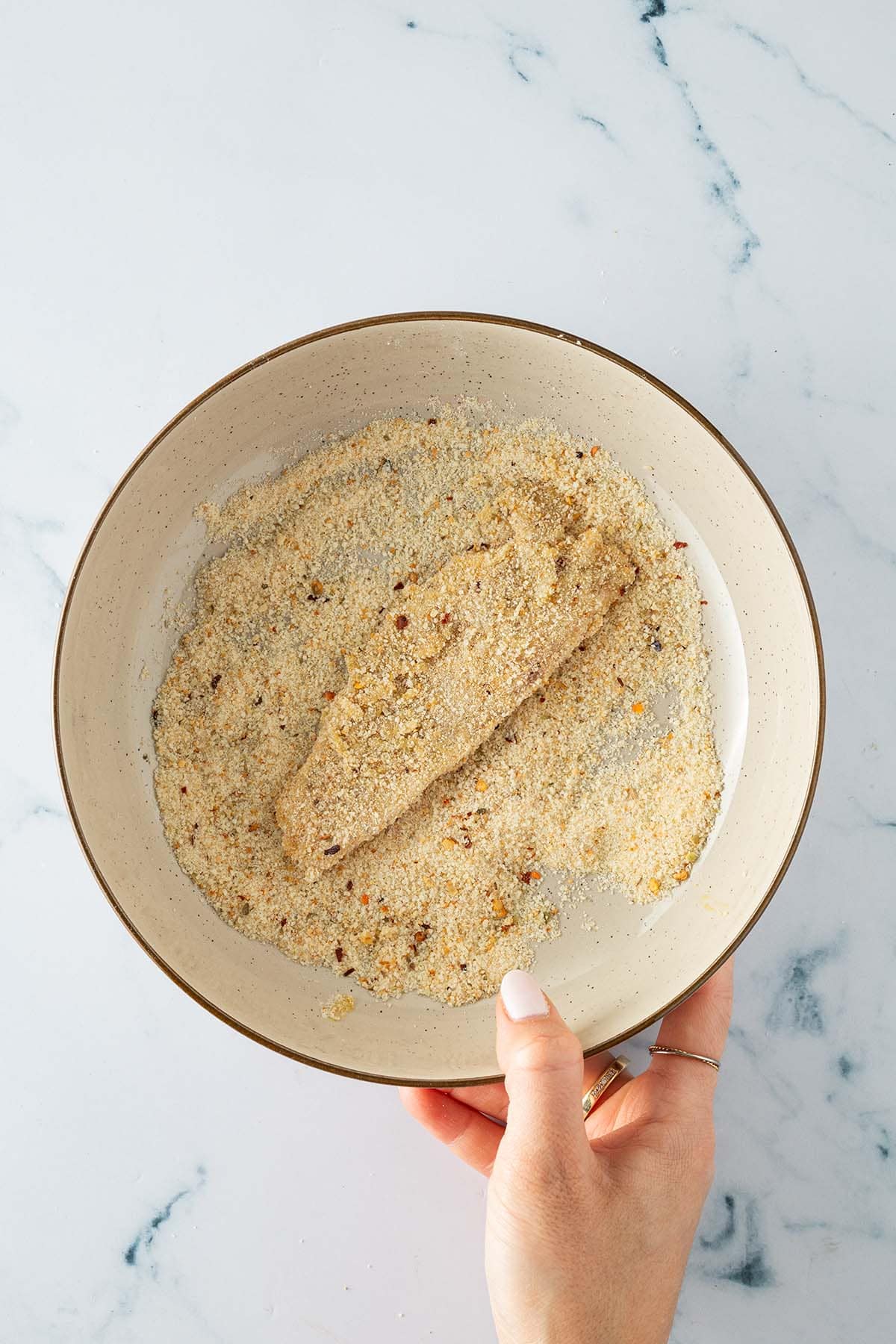 Fischfilet wird in einer Schüssel mit gewürztem Paniermehl gewendet.