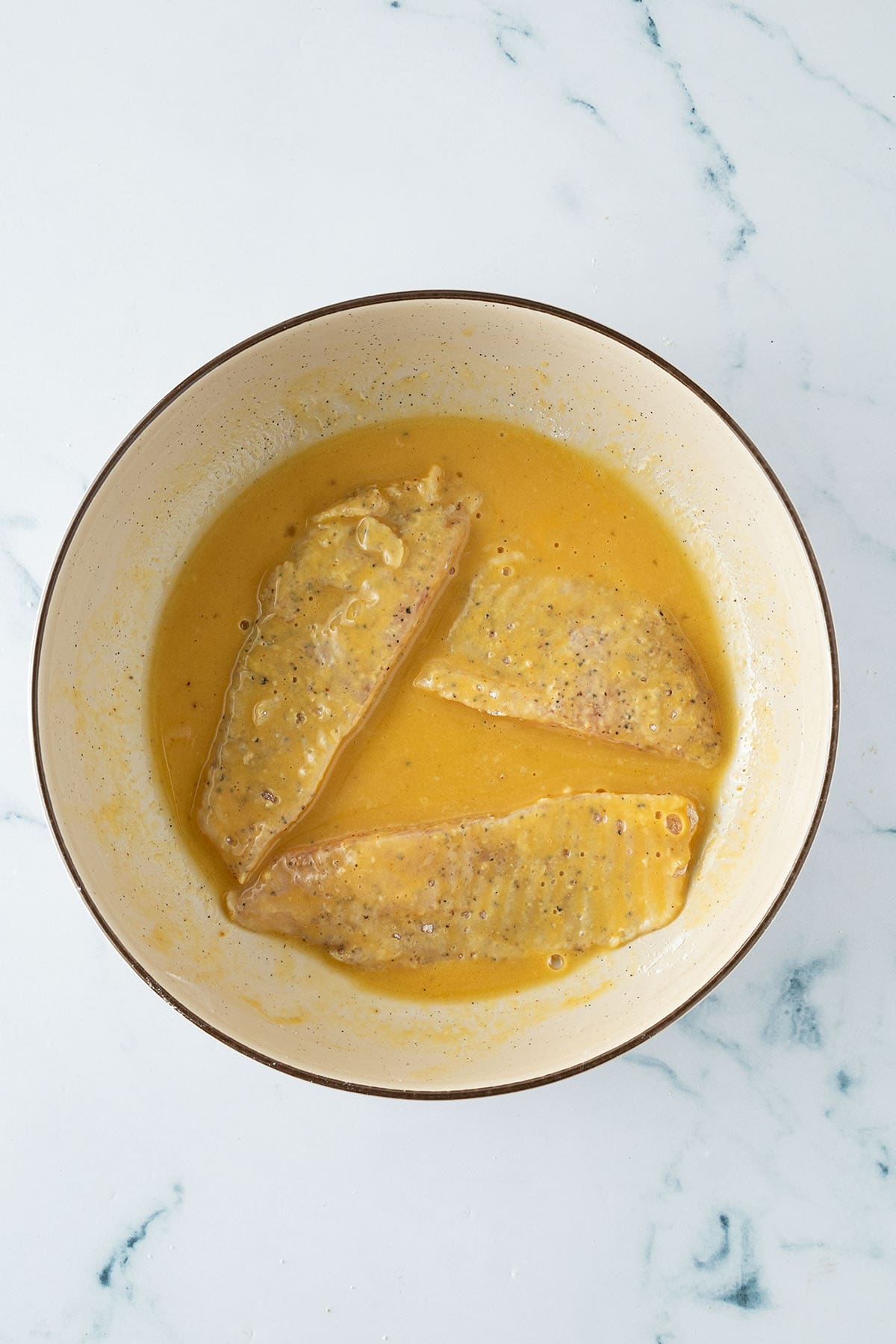 Fischfilets liegen in einer Schüssel mit gewürzter Eimischung zum Panieren.
