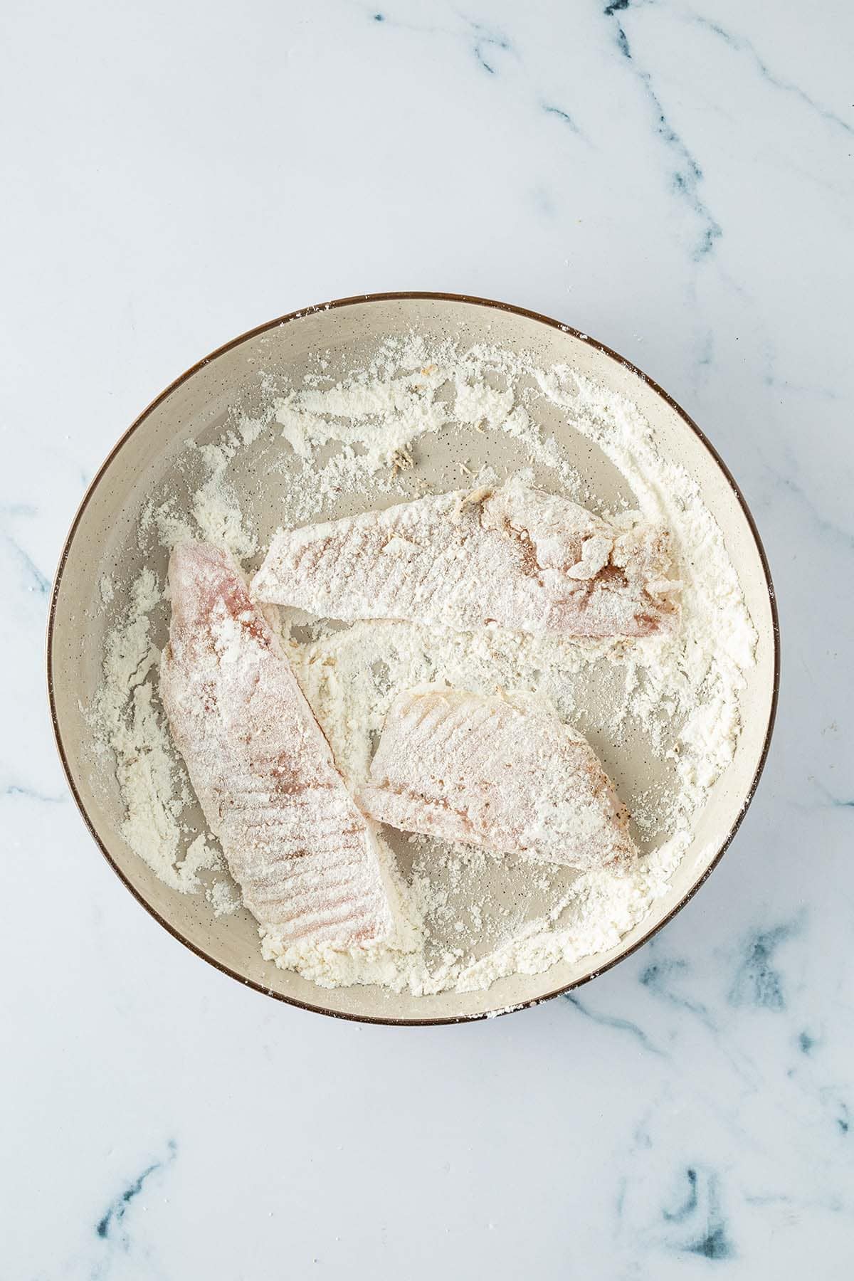 Fischfilets werden in einer Schüssel mit Mehl gewendet.