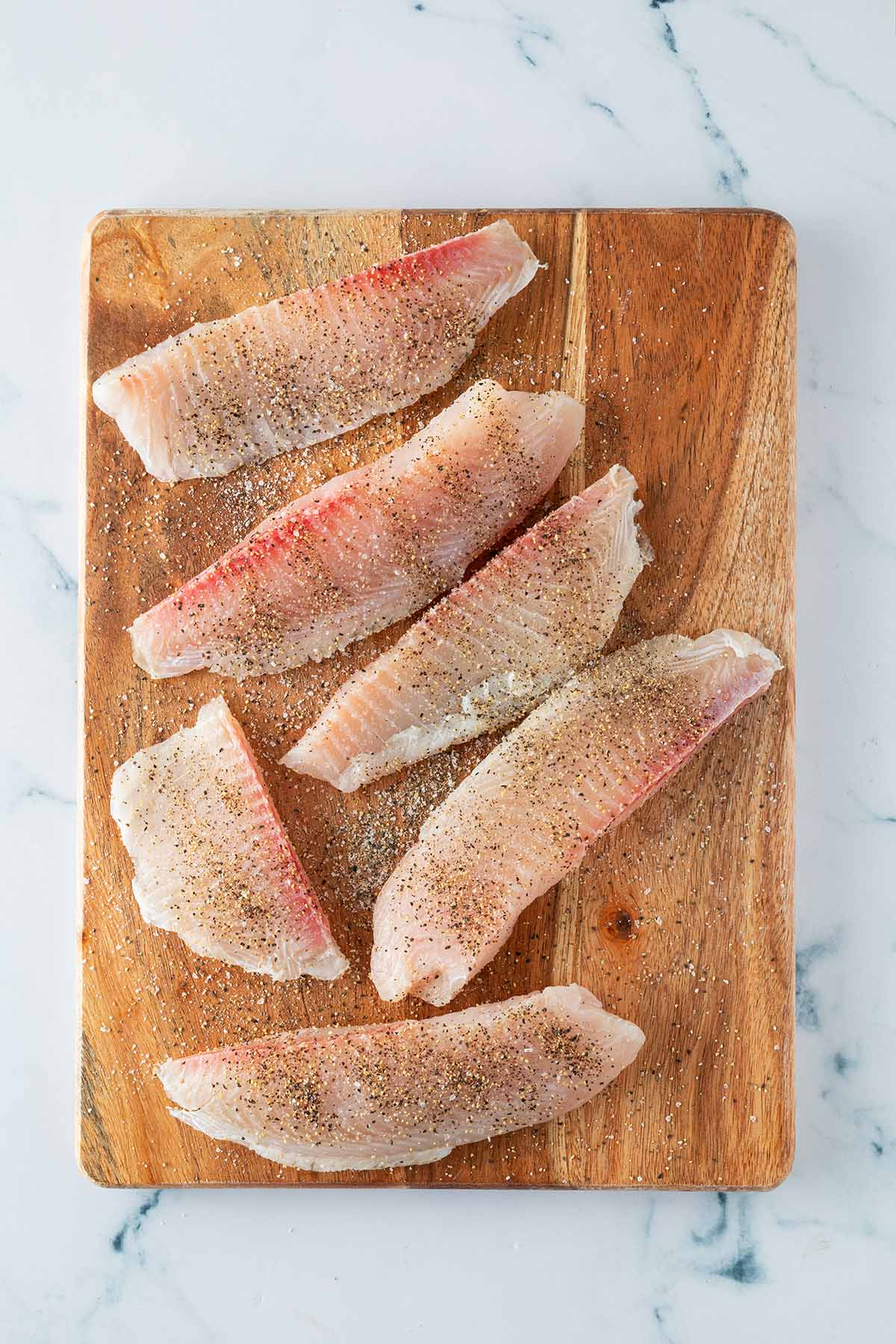 Rohe, gewürzte Fischfilets liegen auf einem Holzbrett, bereit zum Panieren.