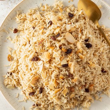 Pilaw Reis auf einem beigen Teller mit Rosinen und Mandeln serviert.