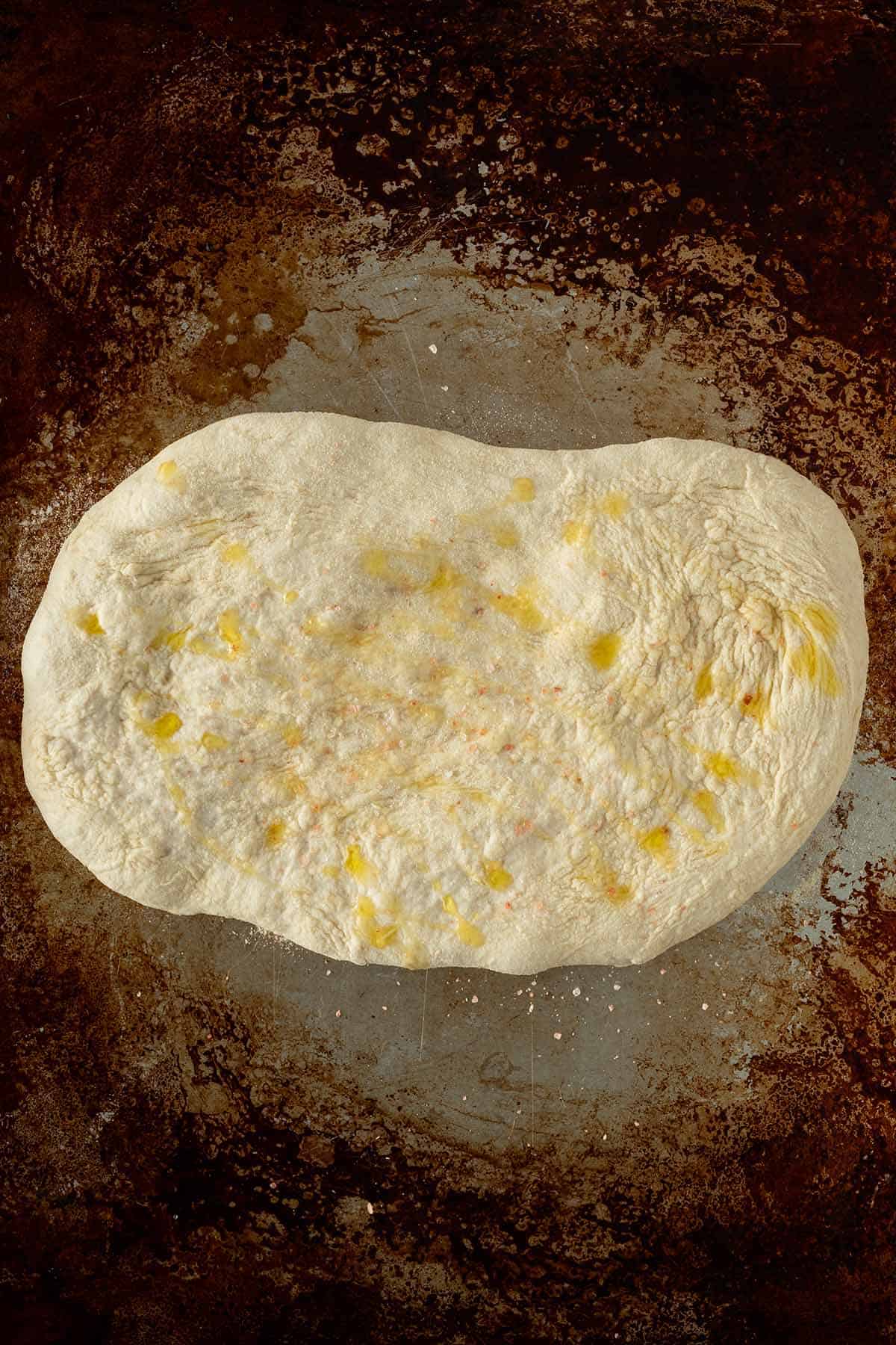 Geformter Pinsa Teig auf dem Backblech direkt vor dem Backen, mit etwas &Ouml;l betr&auml;ufelt.