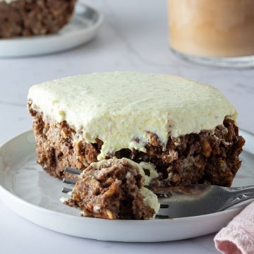 Ein St&uuml;ck Schoko Pistazien Baked Oatmeal auf einem Teller, ein Bissen davon auf einer Gabel mit einem Eiskaffee und einem zweiten St&uuml;ck im Hintergrund.