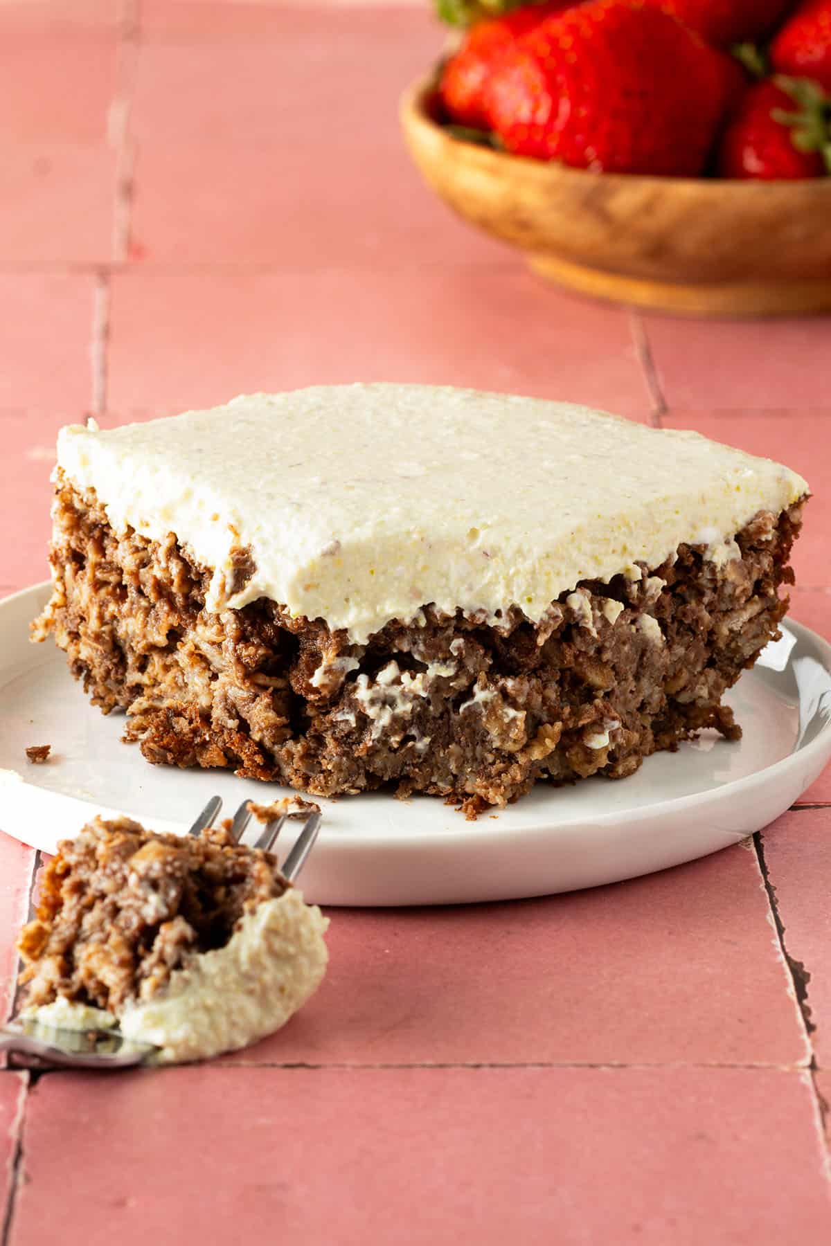 EIn St&uuml;ck Pistazien Baked Oatmeal auf einem Teller, ein St&uuml;ck davon auf einer Gabel liegt davor, eine Sch&uuml;ssel Erdbeeren im Hintergrund.