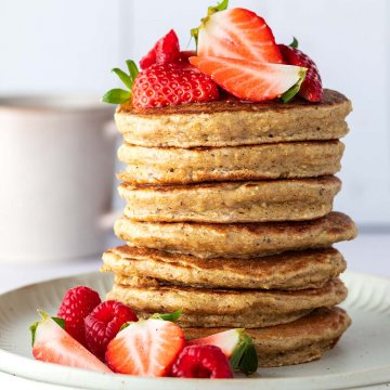 Ein Pancake-Stapel mit frischen Beeren auf einem Teller vor hellem, verschwommenem Hintergrund.