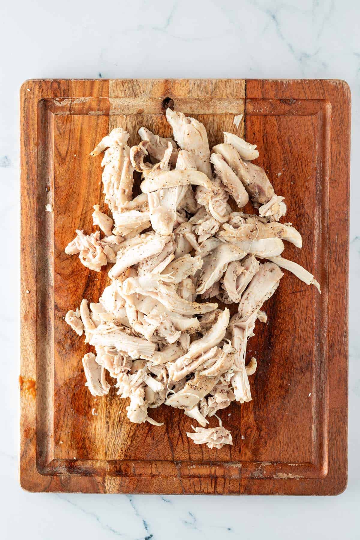 Zartes Pulled Chicken aus H&auml;hnchenbrust und H&auml;hnchenoberkeulen nach dem Zerpfl&uuml;cken auf einem Holzbrett.