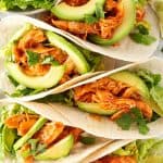 Fünf nebeinander liegende Tacos mit Hähnchen in einer würzigen Sauce, Avocado und Salat.