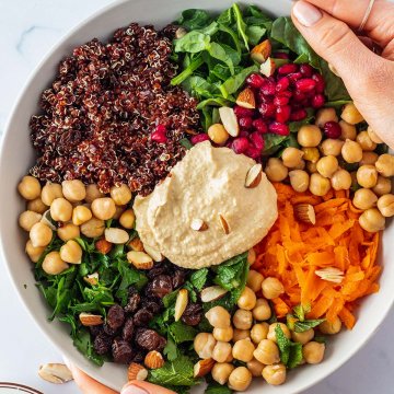 Zwei Hände halten einen Teller, wo die einzelne Komponenten eines Quinoa Salats nebeneinander angerichtet sind.