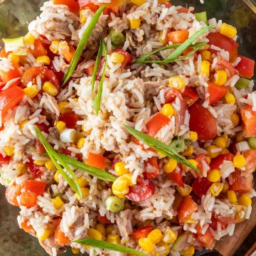 Nahaufnahme von einer Schüssel Reissalat mit Thunfisch, Tomaten, Mais, Paprika und Frühlingszwiebeln.