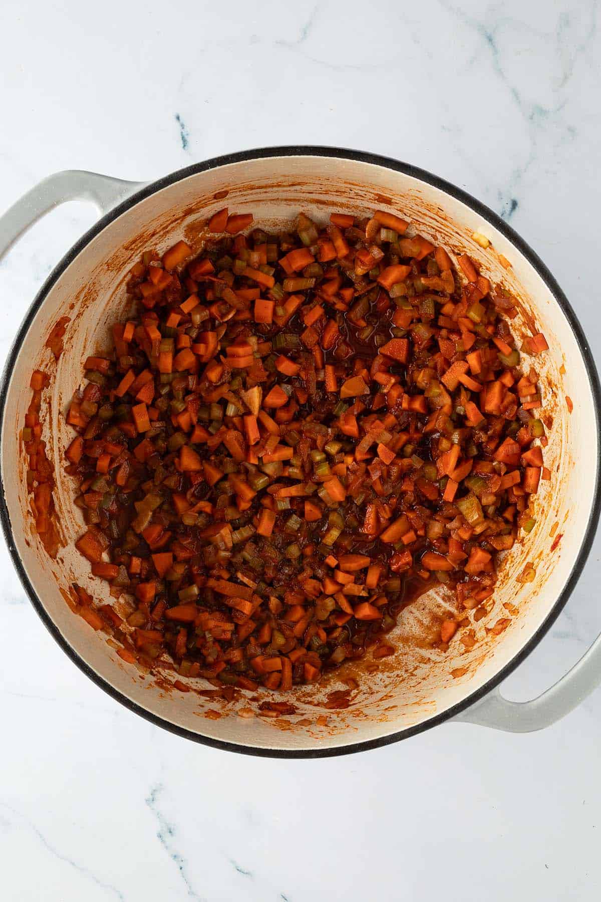 Angebratenes Gemüse mit Tomatenmark in einem Topf mit verkochten Rotwein.