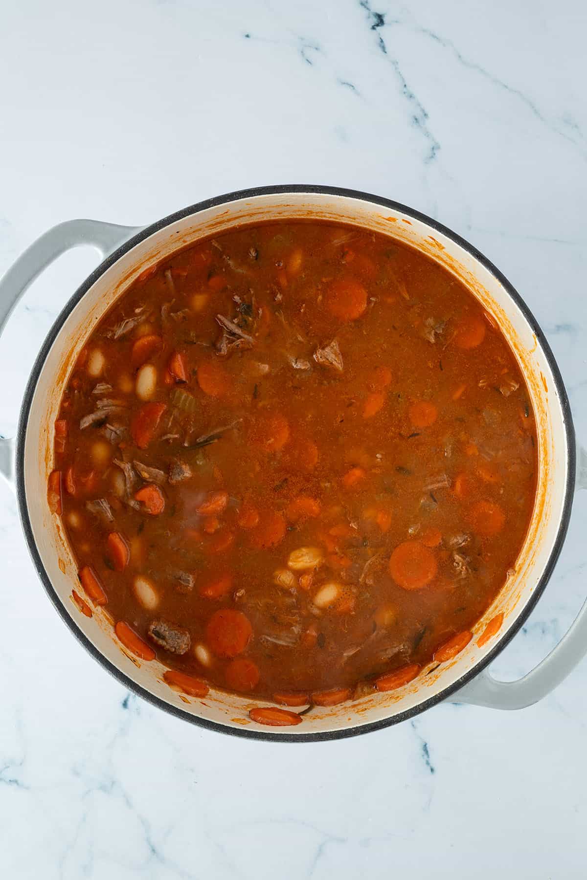 Rindfleischeintopf im Topf, langsam k&ouml;chelnd mit Karotten, wei&szlig;en Bohnen und zarten Fleischst&uuml;cken in tomatiger Br&uuml;he.