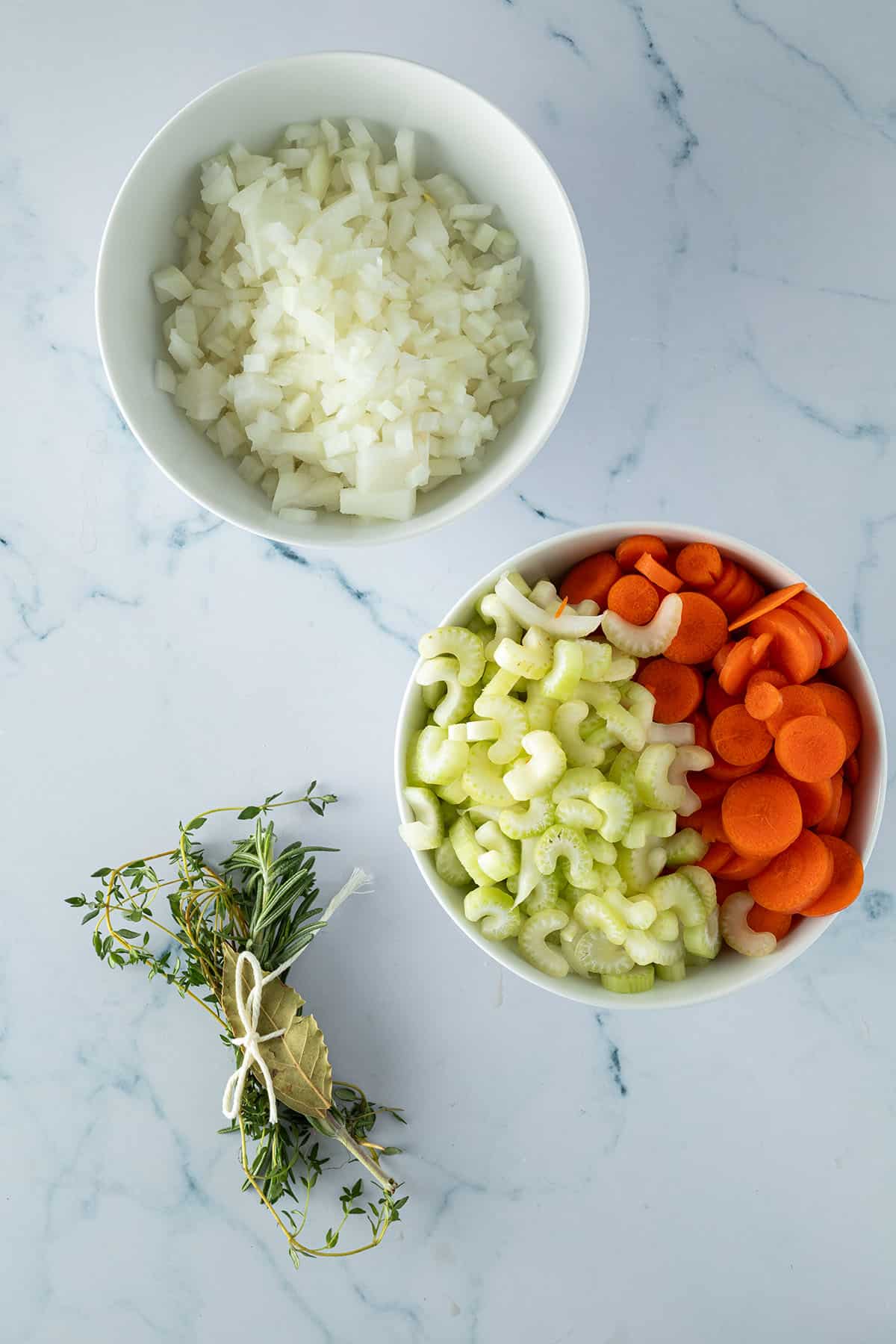 Vorbereitete Zutaten f&uuml;r Rindfleischeintopf: gew&uuml;rfelte Zwiebeln, geschnittener Sellerie, Karotten und ein Kr&auml;uterbund.