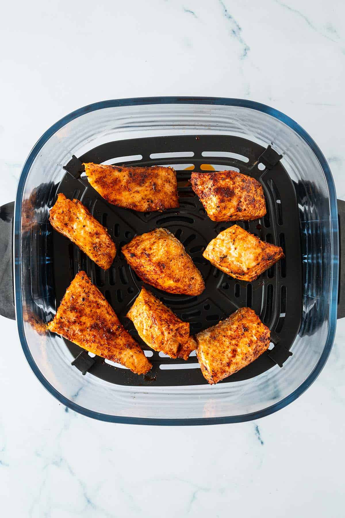 Gew&uuml;rzte Lachsfiletst&uuml;cke im Airfryer-Korb, goldbraun gegart.