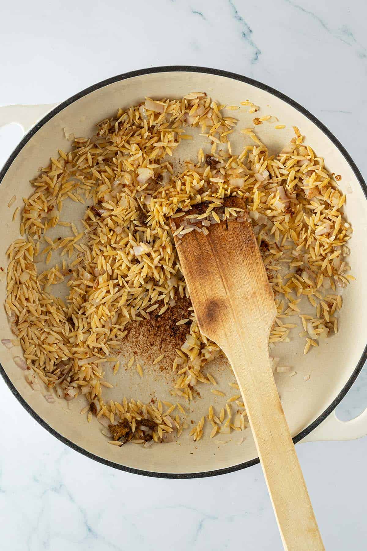 Orzo-Nudeln mit Zwiebeln in der Pfanne anger&ouml;stet und umger&uuml;hrt.