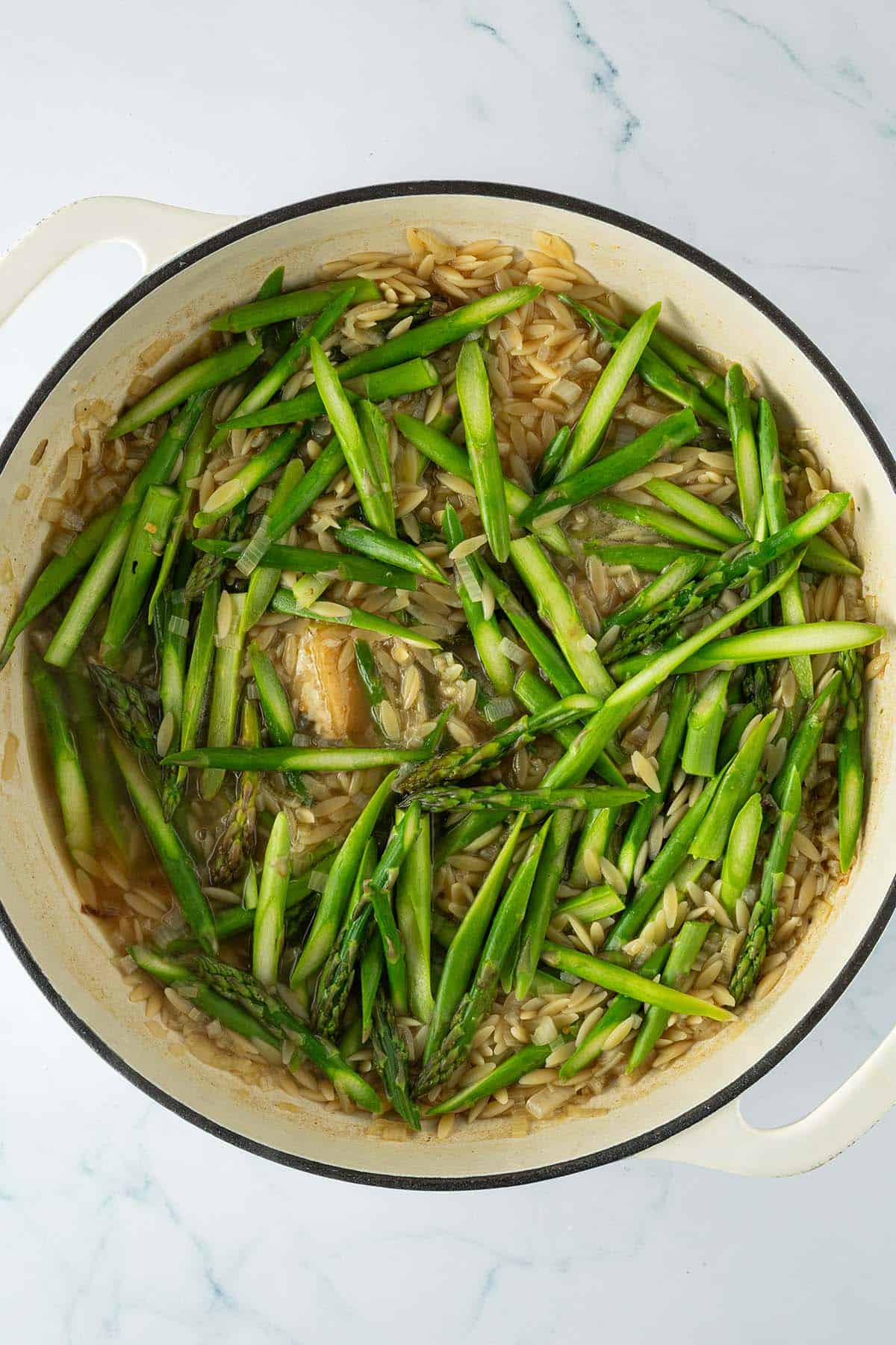 Orzo mit gr&uuml;nem Spargel in der Pfanne, wird mit einem Holzl&ouml;ffel ger&uuml;hrt.