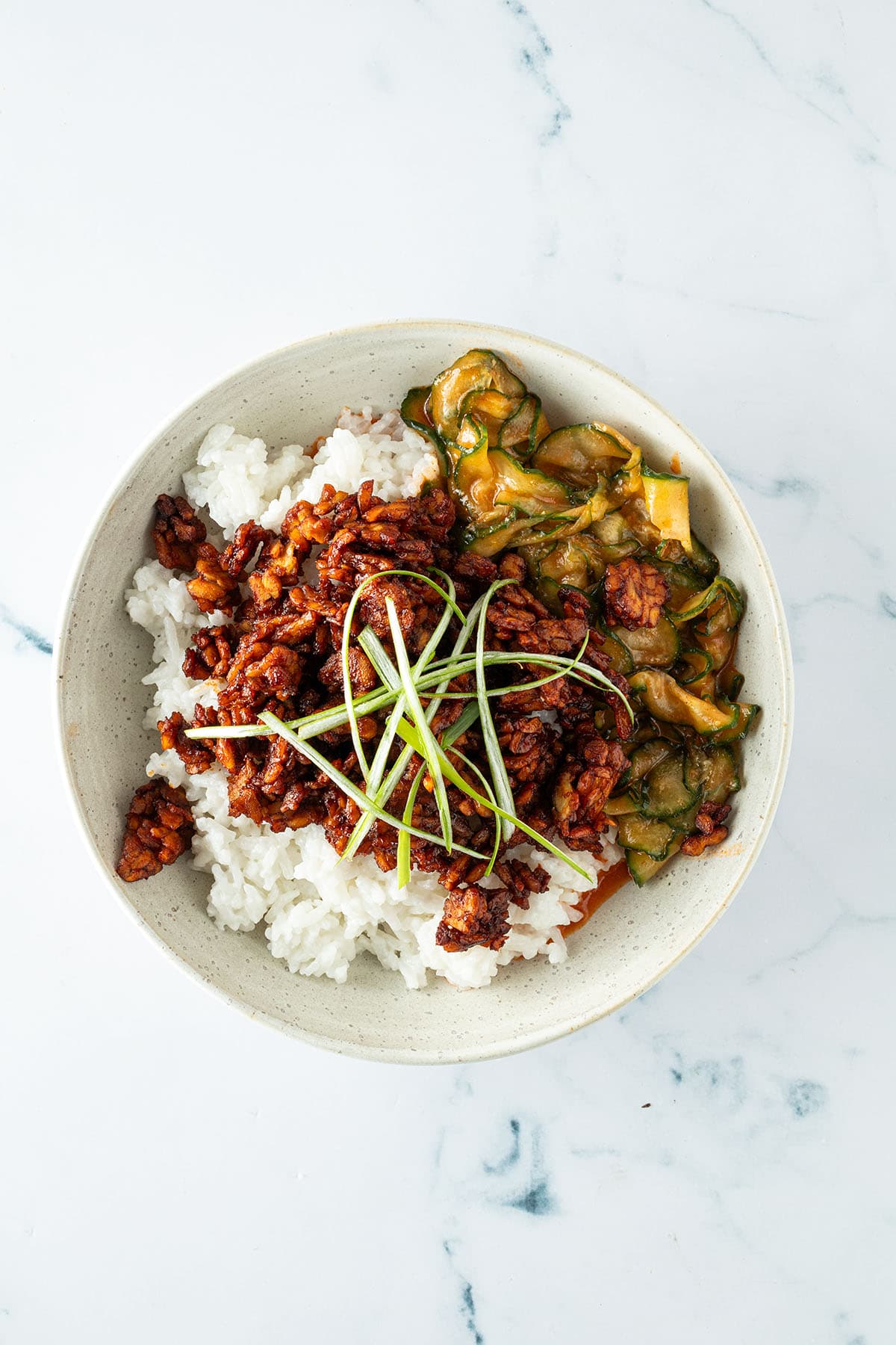 Kokosreis, asiatischer Gochujang Miso Gurkensalat und Sticky Tempeh in einer Sch&uuml;ssel mit Fr&uuml;hlingszwiebeln als Deko.