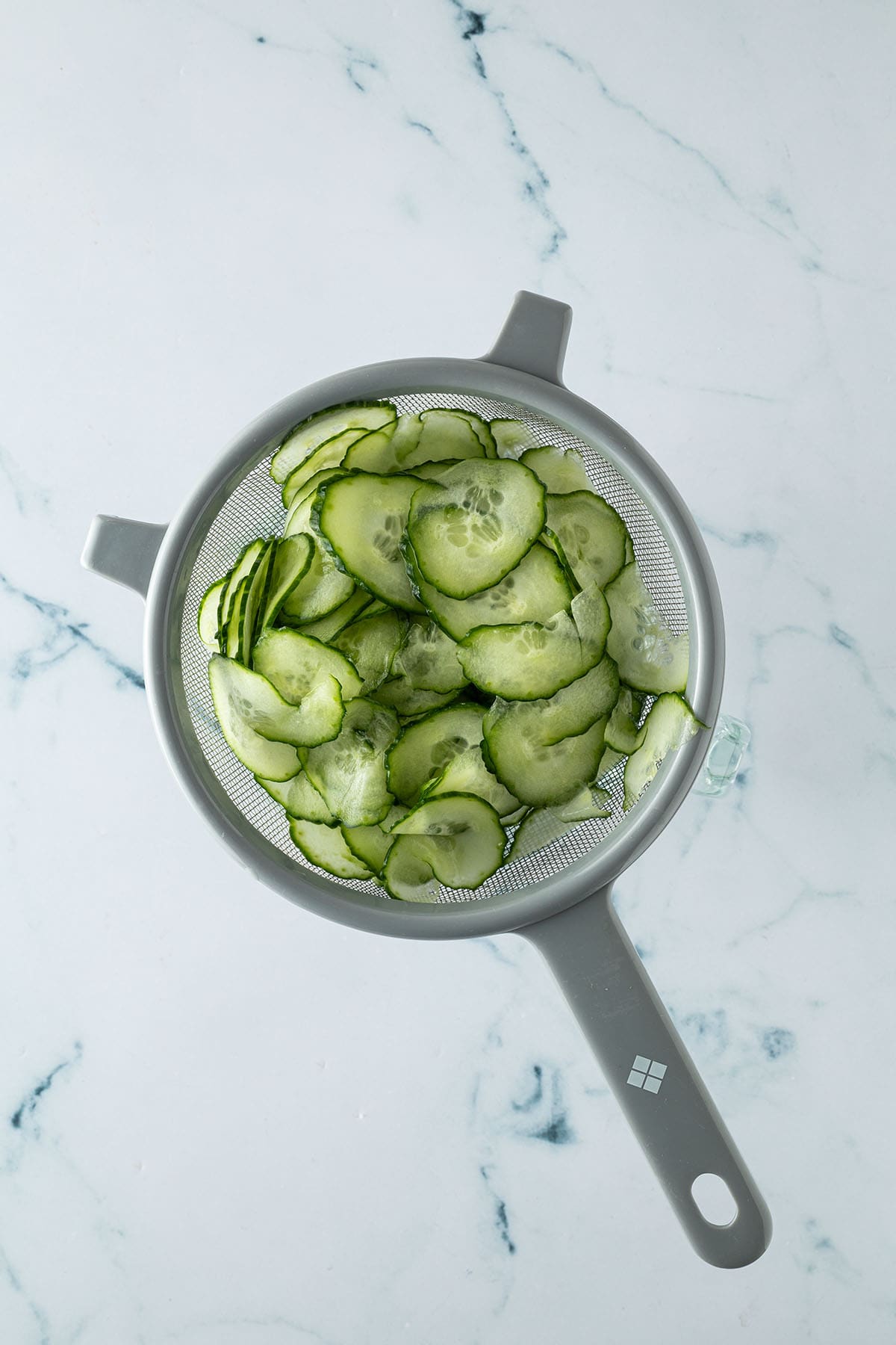 In d&uuml;nne Scheiben geschnittene Gurke in einem Seiher zum Entw&auml;ssern.