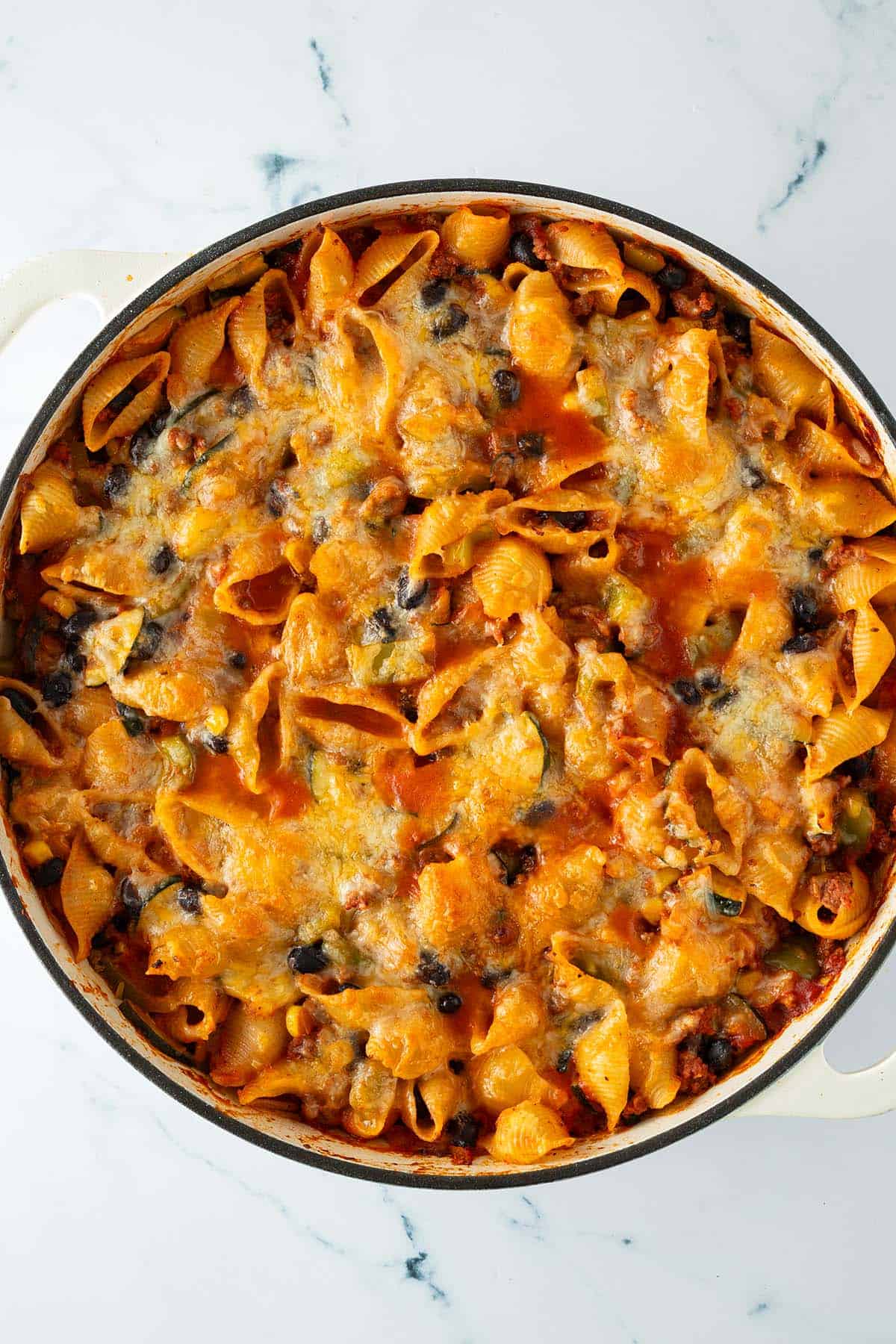 Nahaufnahme eines frisch überbackenen Nudelauflaufs mit geschmolzenem Käse, Bohnen und Pasta in einer hellen Auflaufform.