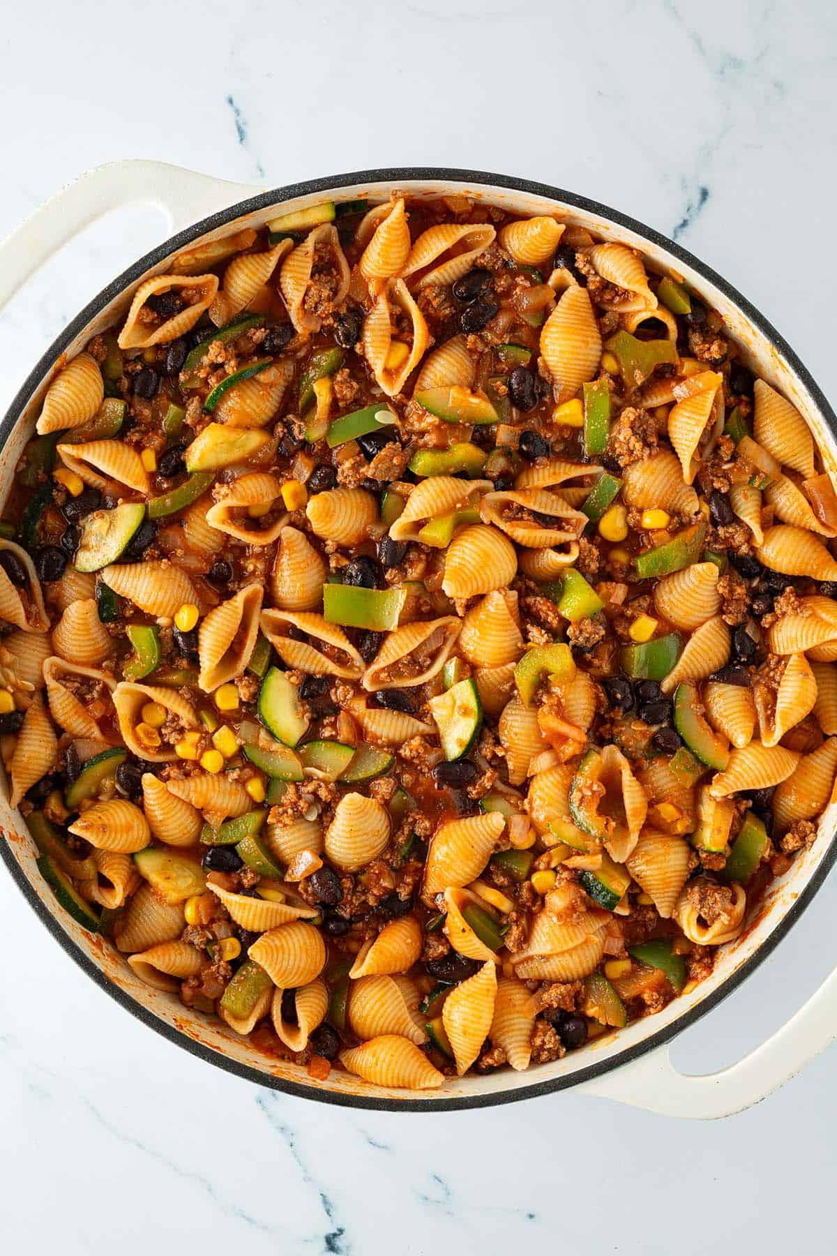 Große Pfanne mit gekochten Muschelnudeln, Hackfleisch, Zucchini, Mais und schwarzen Bohnen in würziger Tomatensauce.