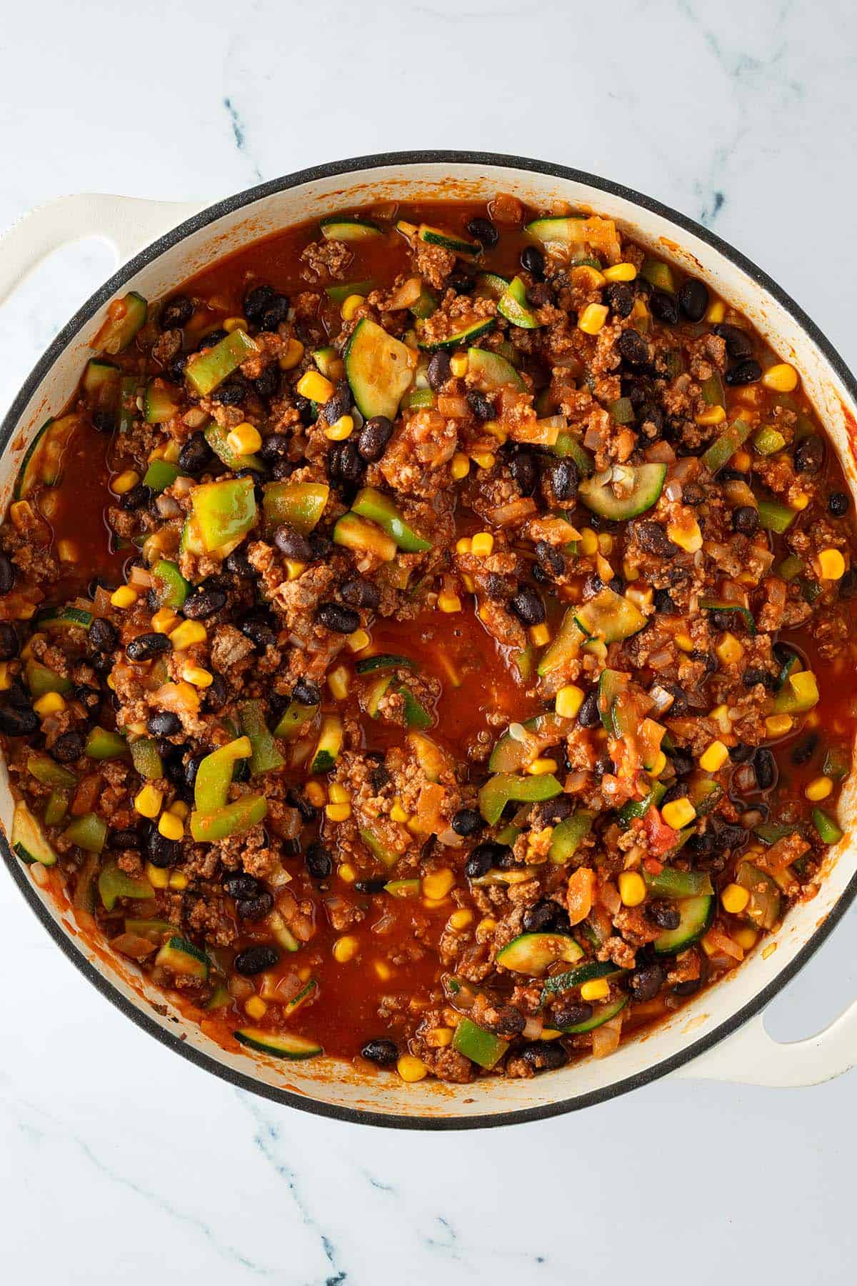 Pfanne mit köchelnder Tex-Mex Hackfleisch-Gemüse-Sauce aus Zucchini, Paprika, Mais und schwarzen Bohnen in Tomatensauce.