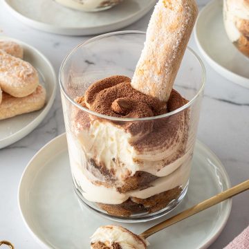 Tiramisu im Glas geschichtet mit Löffelbiskuit, im Hintergrund mehr Gläser mit Tiramisu und Löffelbiskuits.
