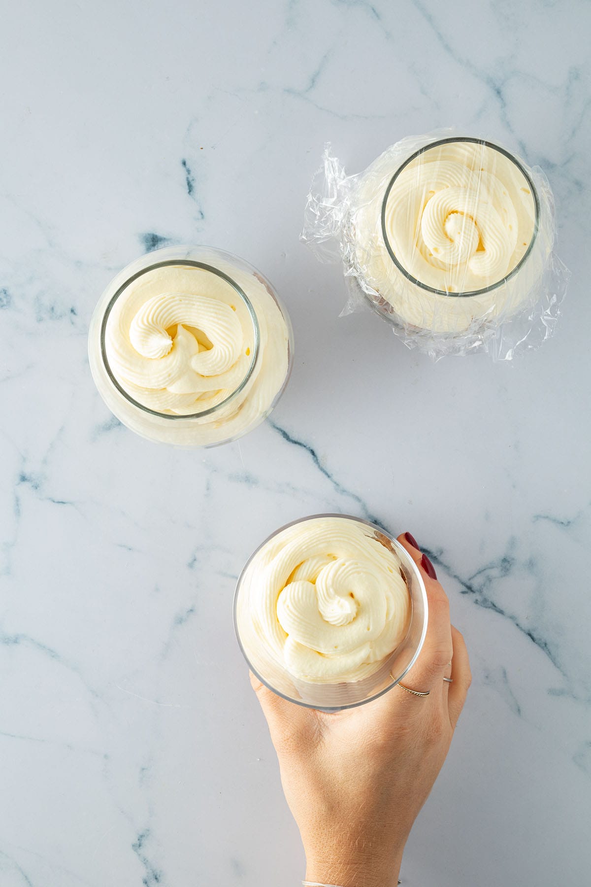 Gläser mit frisch aufgespritzter Mascarpone-Creme, eines leicht mit Folie abgedeckt.“