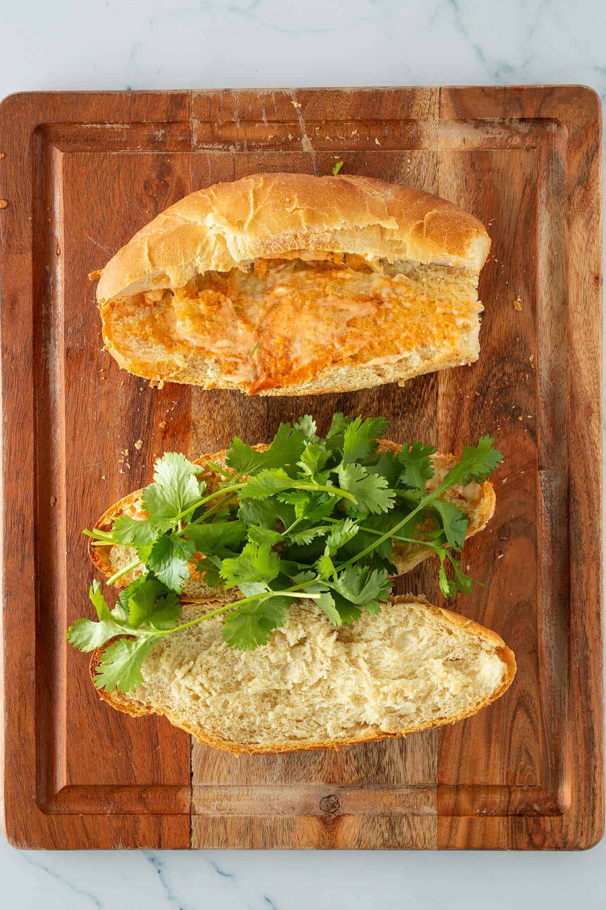 Zwei Banh Mi Baguette auf einem Holzbrett mit Sriracha Mayo und Koriander belegt.