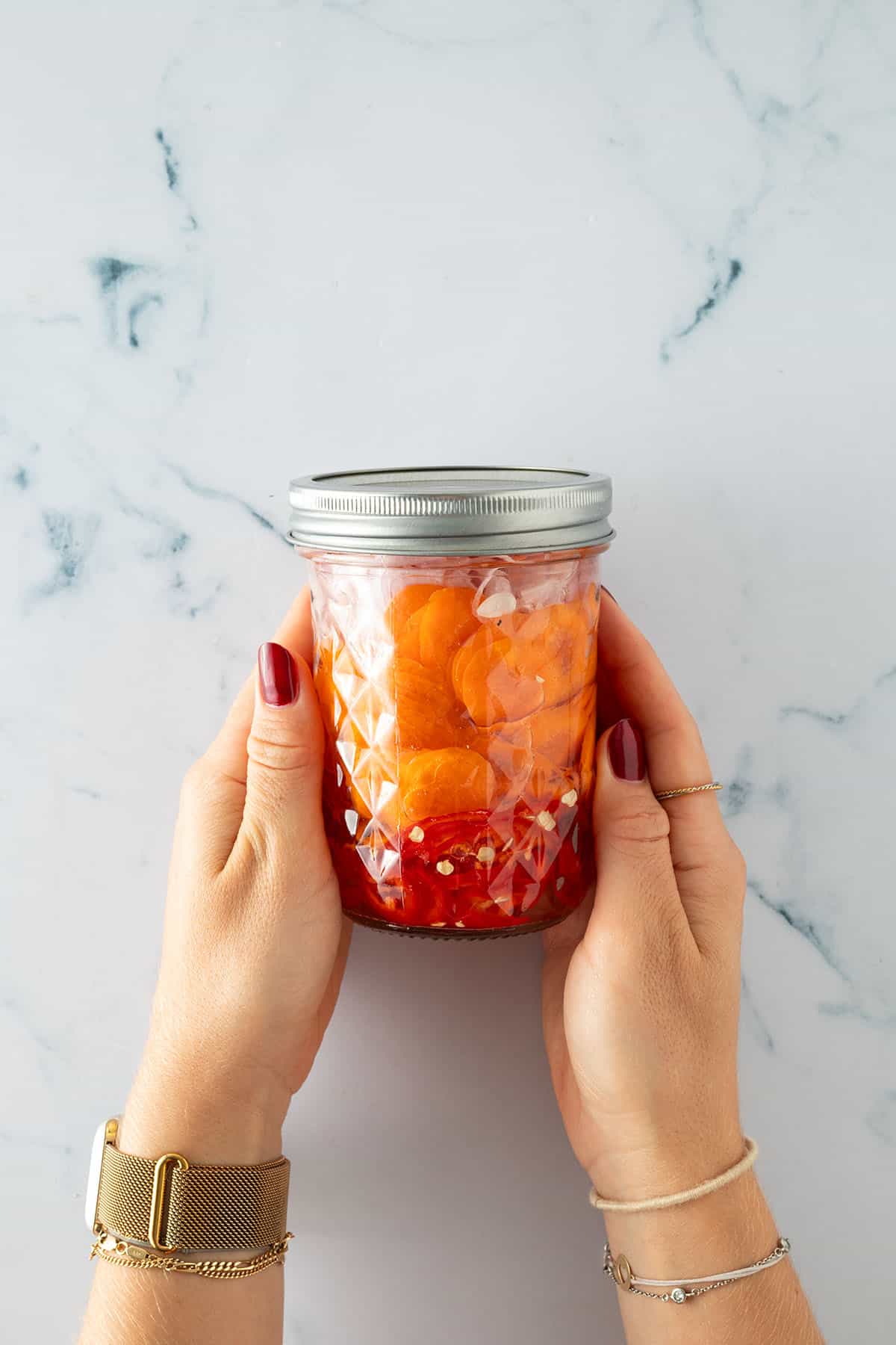 Hände halten ein Glas mit eingelegten Karotten und Chili in einer Essigflüssigkeit.