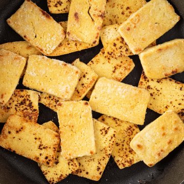 Nahaufnahme von knusprig angebratenen Tofu-Scheiben in einer Gusseisenpfanne.