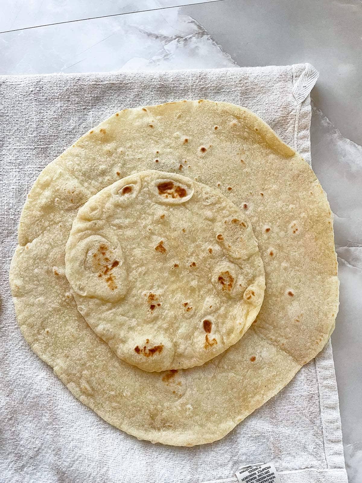 Ein gro&szlig;er und ein kleiner selbstgemachter Tortilla liegen &uuml;bereinander auf einem Geschirrtuch.