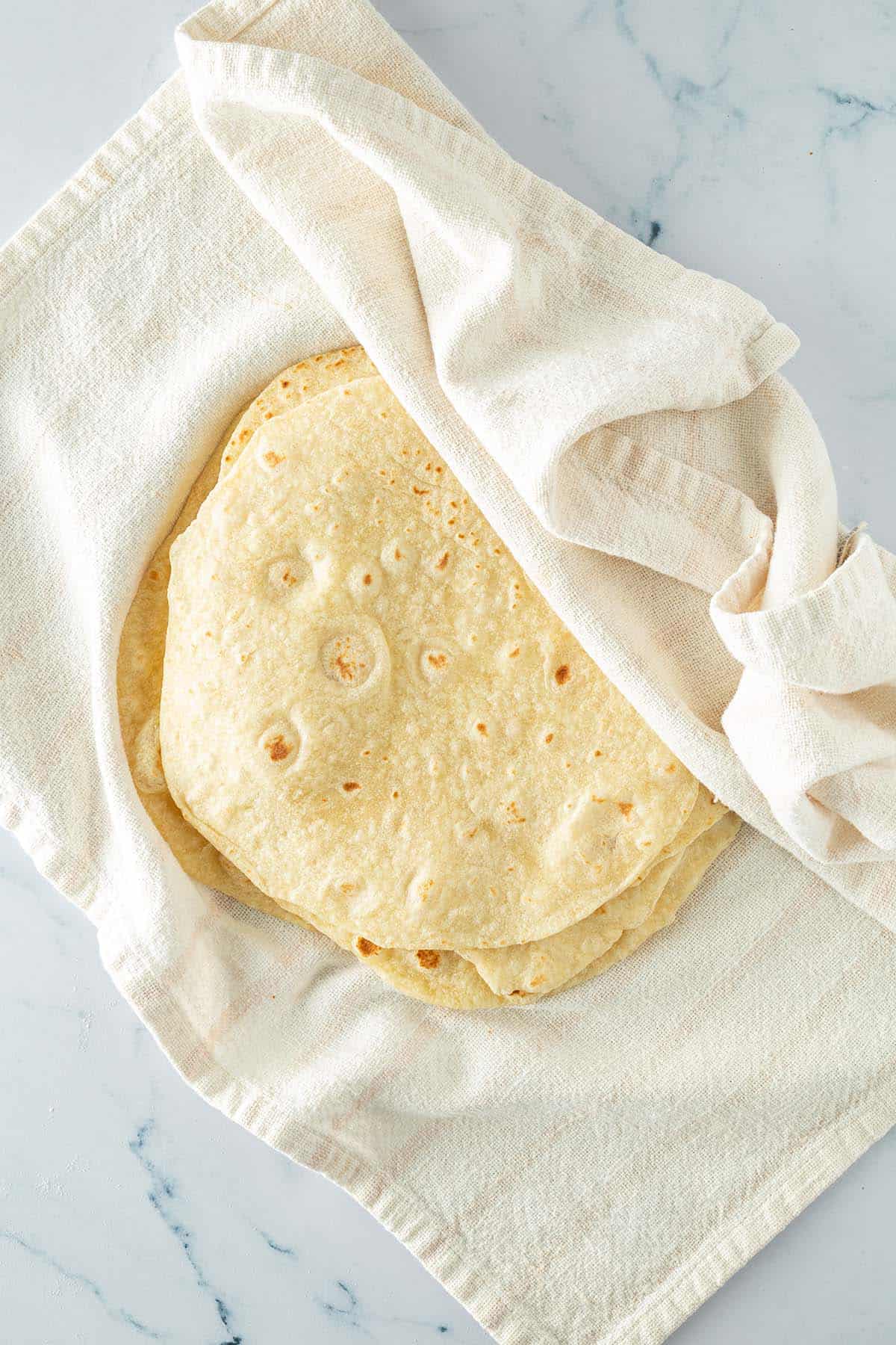 Aufeinander gestapelte, selbstgemachte Weizen Tortillas eingewickelt in einem Geschirrtuch.