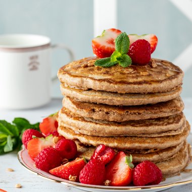 Stapel vegane Pancakes mit Himbeeren und Erdbeeren sowie frischer Minze und Ahornsirup serviert
