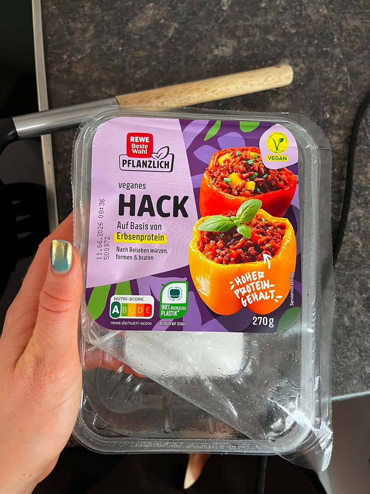 Eine Hand h&auml;lt eine leere Packung von einem veganen Hackfleischersatz von der Rewe Eigenmarke.
