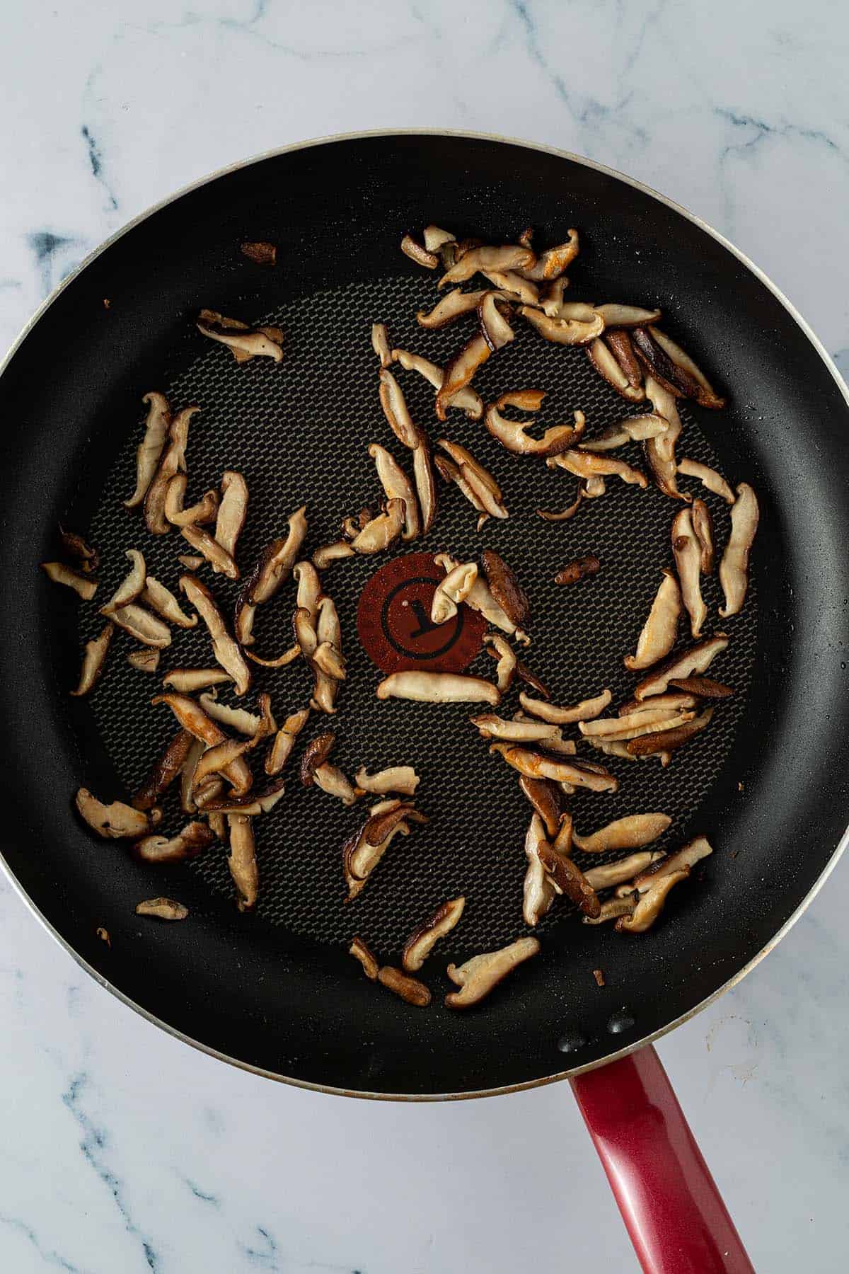 In Scheiben geschnittene Shiitakepilze werden in einer beschichteten Pfanne angebraten.