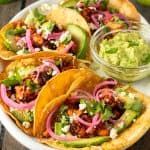 Vier vegetarische Tacos mit Tofu, Avocado und Zwiebeln auf einem Teller.