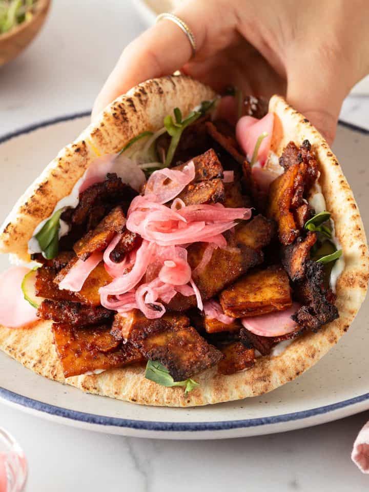 Hand hält ein vegetarischen Tofu Döner mit eingelegten Zwiebeln, Gurke und Sprossen.