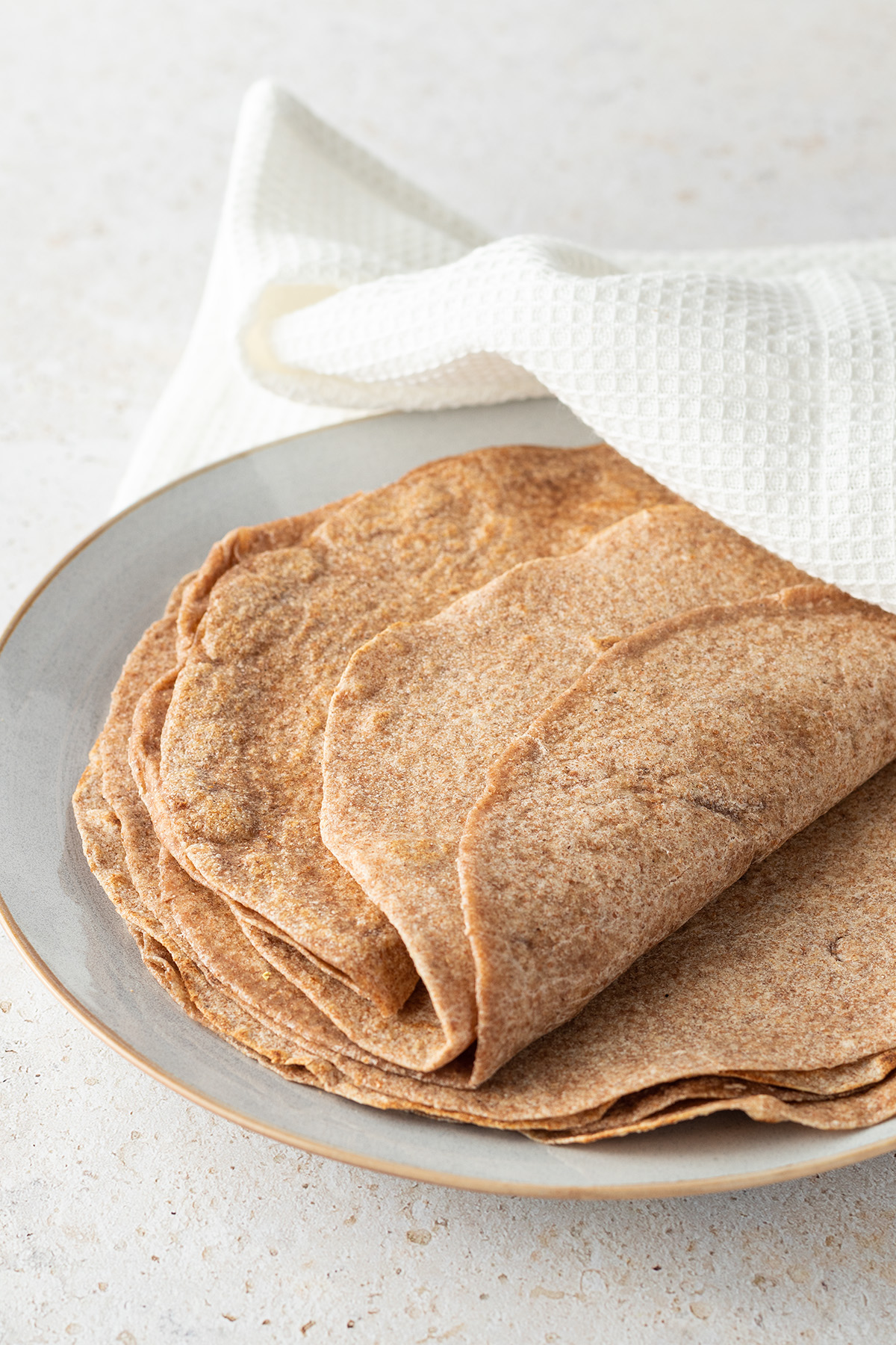 Ein Stapel aus Tortilla Wraps auf einem Teller, halb mit einem weißen Geschirrtuch bedeckt.