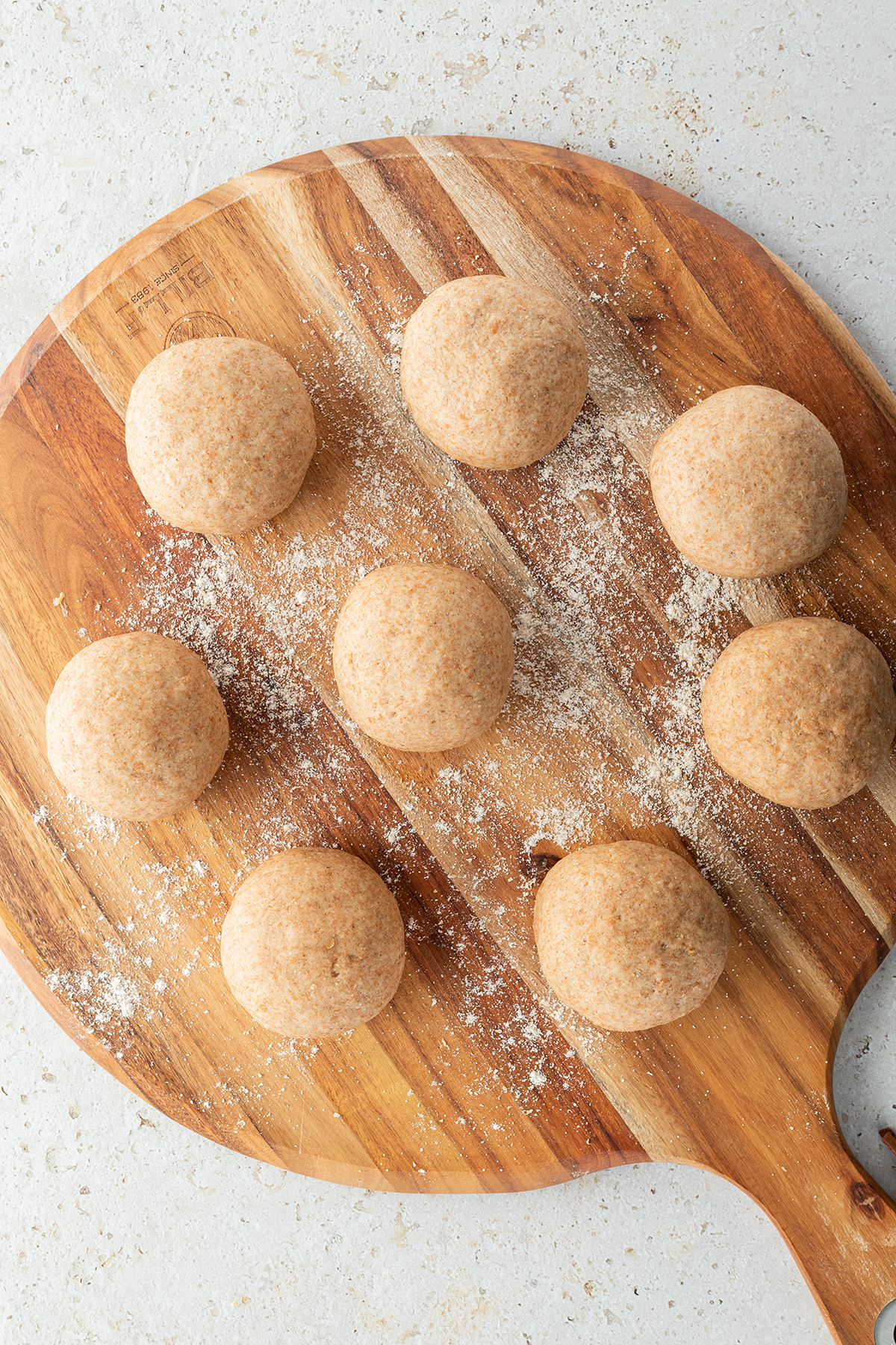 Acht gleich große Teigbällchen auf einem Holzbrett,