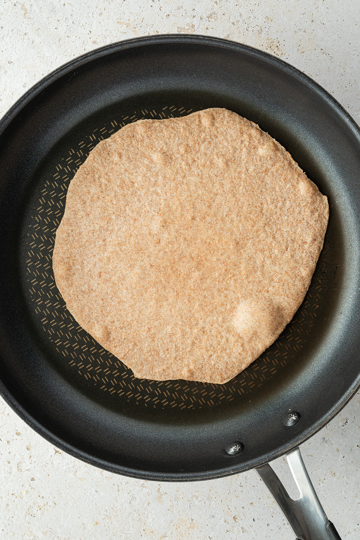 Tortilla Wrap in einer großen Beschichteten Pfanne, auf dessen Oberseite sich kleinere und größere Blasen gebildet haben.