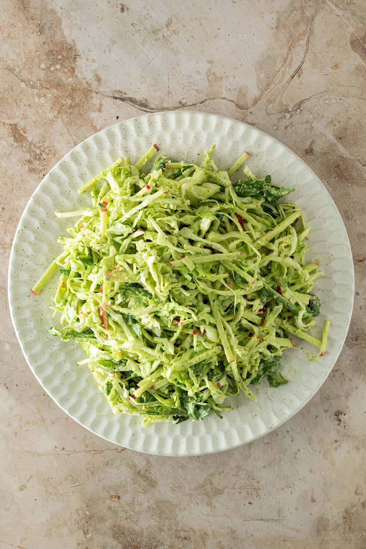 Wei&szlig;kohlsalat mit Apfel, Rucola und einem gr&uuml;nen Dressing auf einem gro&szlig;en Teller auf einem Steinuntergrund.