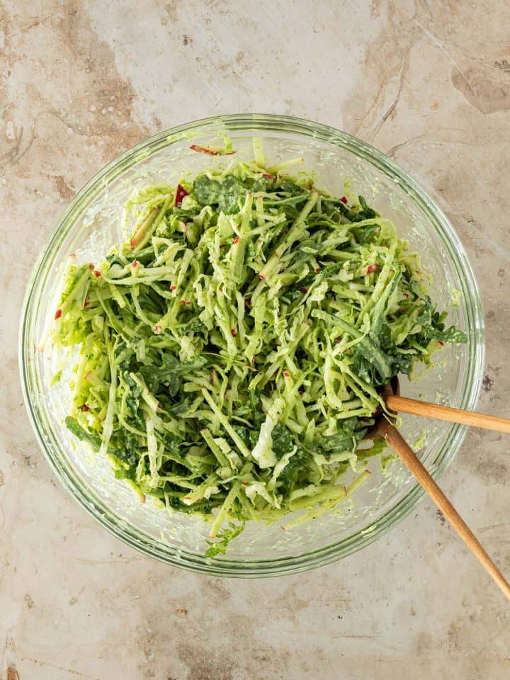 Eine Sch&uuml;ssel mit Wei&szlig;kohlsalat mit Apfel, Rucola und gr&uuml;nem Dressing auf einem Steinuntergrund mit Salatbesteck.